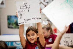 student holding up whiteboard with a math problem