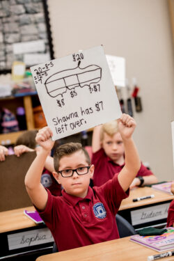 student holding up whiteboard with a math problem