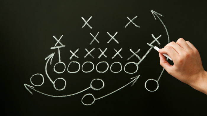 hand writing out a football play on a chalk board