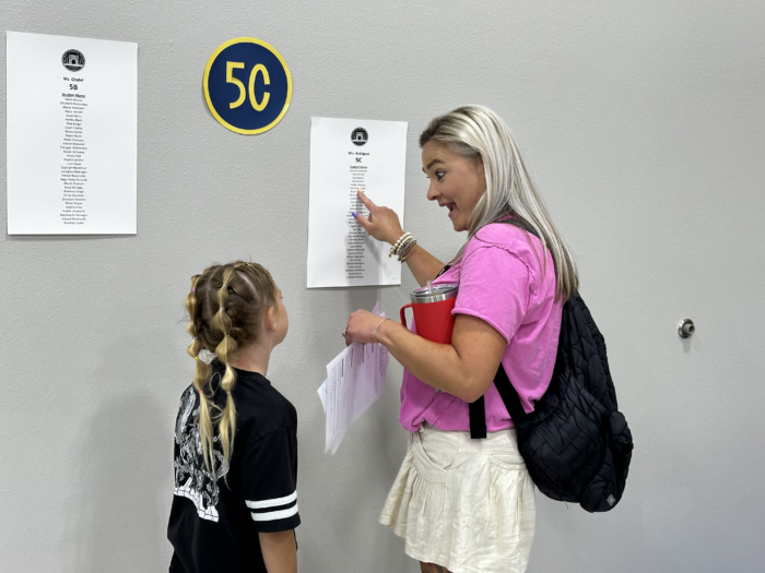 A parent and child reading a classroom roster on the wall