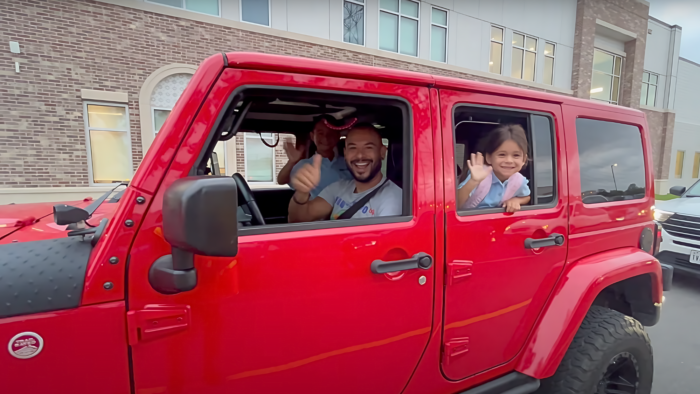 Man in a red jeep dropping his kids off to school.