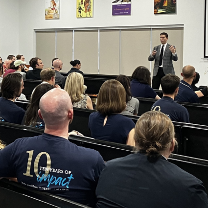 Large group of teachers seated in an auditorium with a speaker up front.