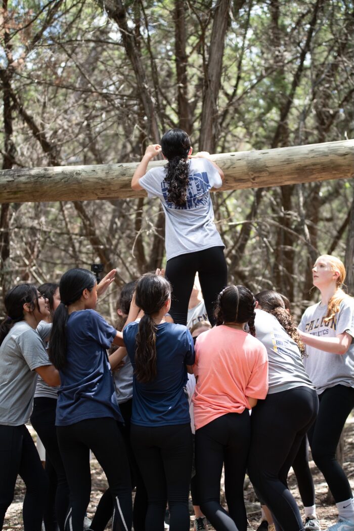 group of students lifting a female student up to a log