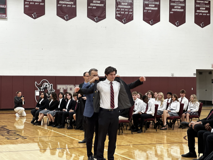 Student putting a blazer on with the help of a teacher