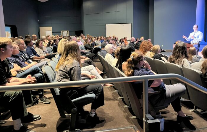 Large group of teachers seated in an auditorium with a speaker up front.