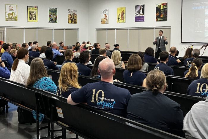 Large group of teachers seated in an auditorium with a speaker up front.