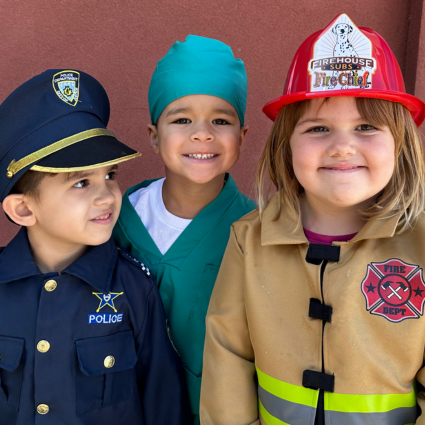 Three preschoolers dressed as a policeman, a medical professional, and a firefighter