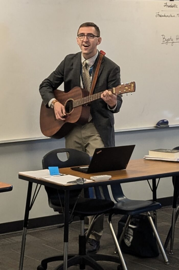 Mr. Byerly singing and playing guitar in front of a classroom