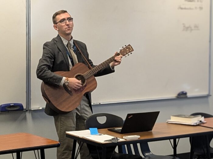 Mr. Byerly singing and playing guitar in front of a classroom