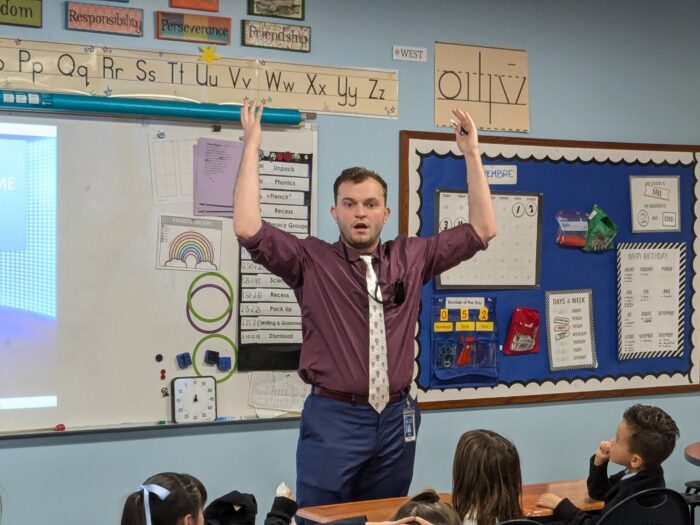 Henry Schreiber with his hands raised above his head in front of his classroom