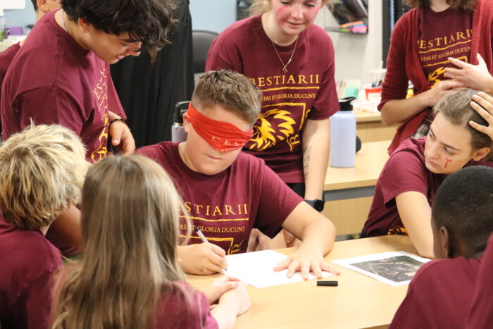 Blindfolded student drawing while being surrounded by students.