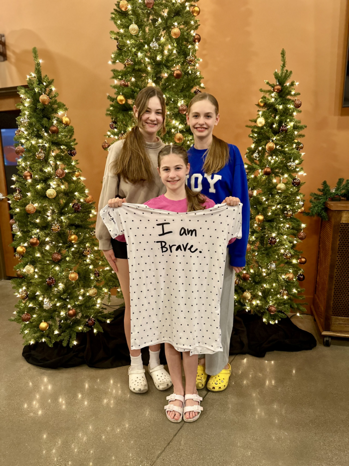 Three girls holding a hospital gown in front of Christmas trees