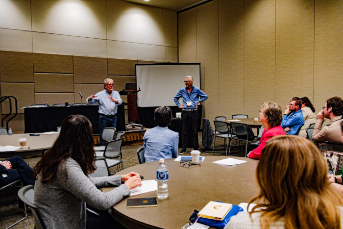 Attendees at a workshop listening to speakers in the front of the room.