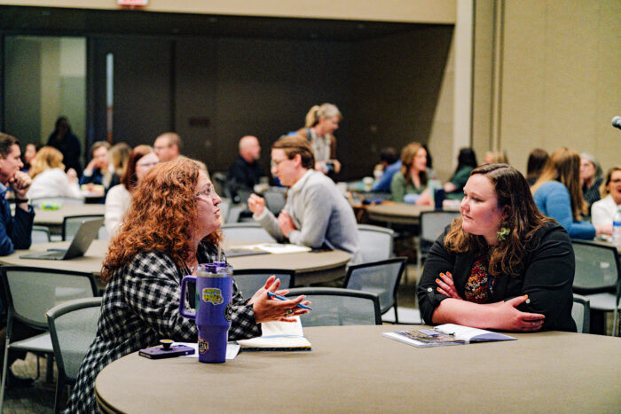 Two women talking at a table with others behind them