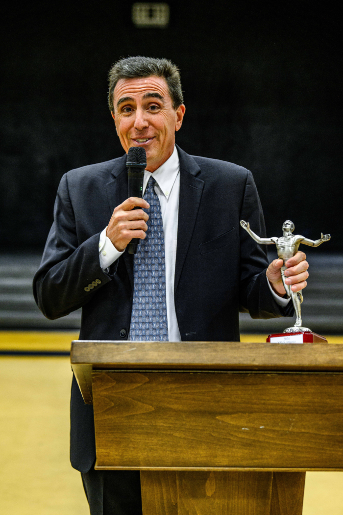 Coach Webdale holding a microphone and holding a trophy