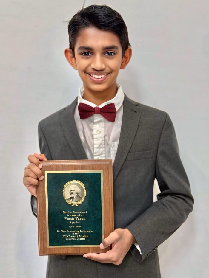 Student wearing suit and bow tie holding a 2nd place plaque