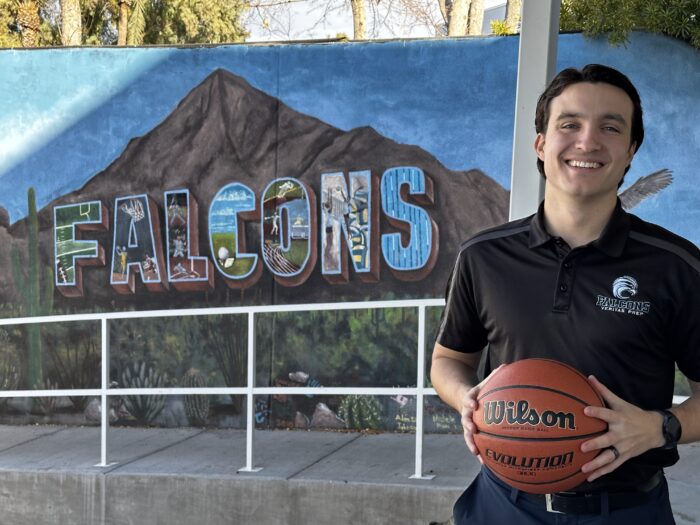 AD Chase Beebe posing with a basketball in front of a mural that reads, "FALCONS"