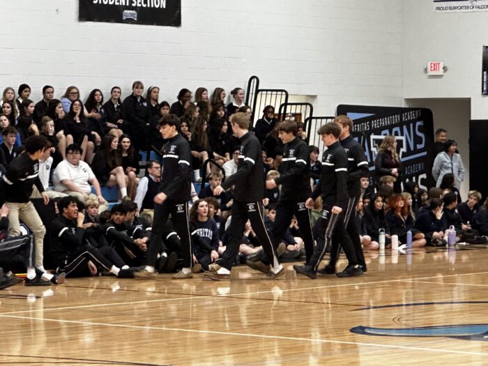 basketball players walking in front of bleachers filled with students in a gym.