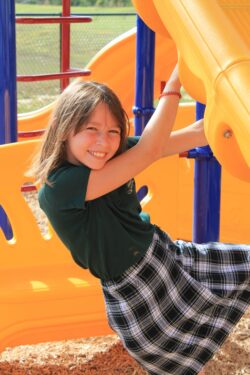 Girl in uniform playing on an outdoor slide.