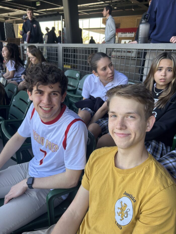 Two male students sitting in the stands of a baseball fields