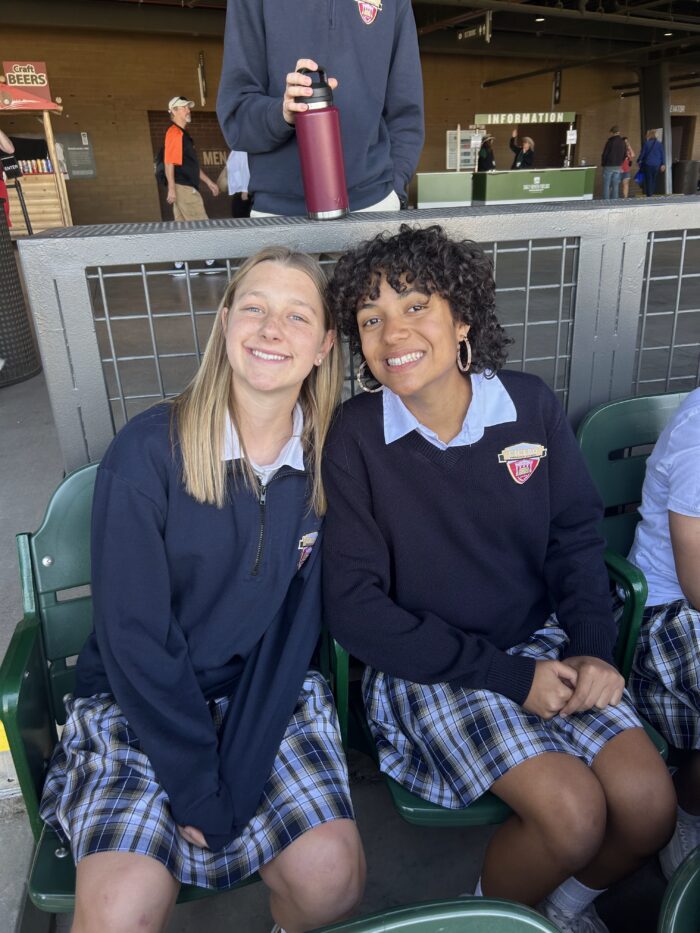 Two female students sitting in the stands of a baseball field